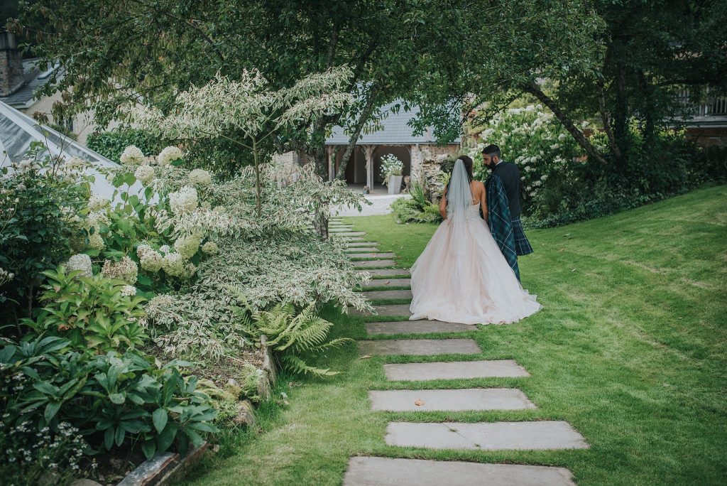 back view of bride and groom in kilt walking in Ever After gardens