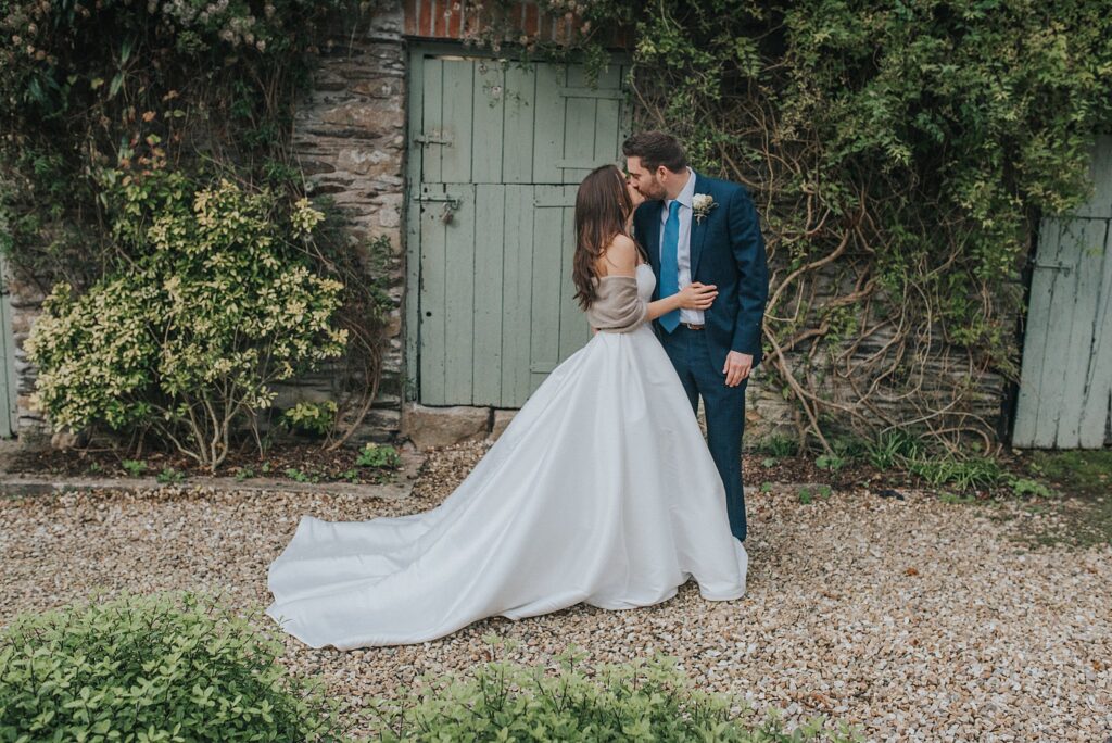 October elopements at Ever After with bride in long white dress kissing groom dressed in blue suit in front of old wooden pale green painted barn doors