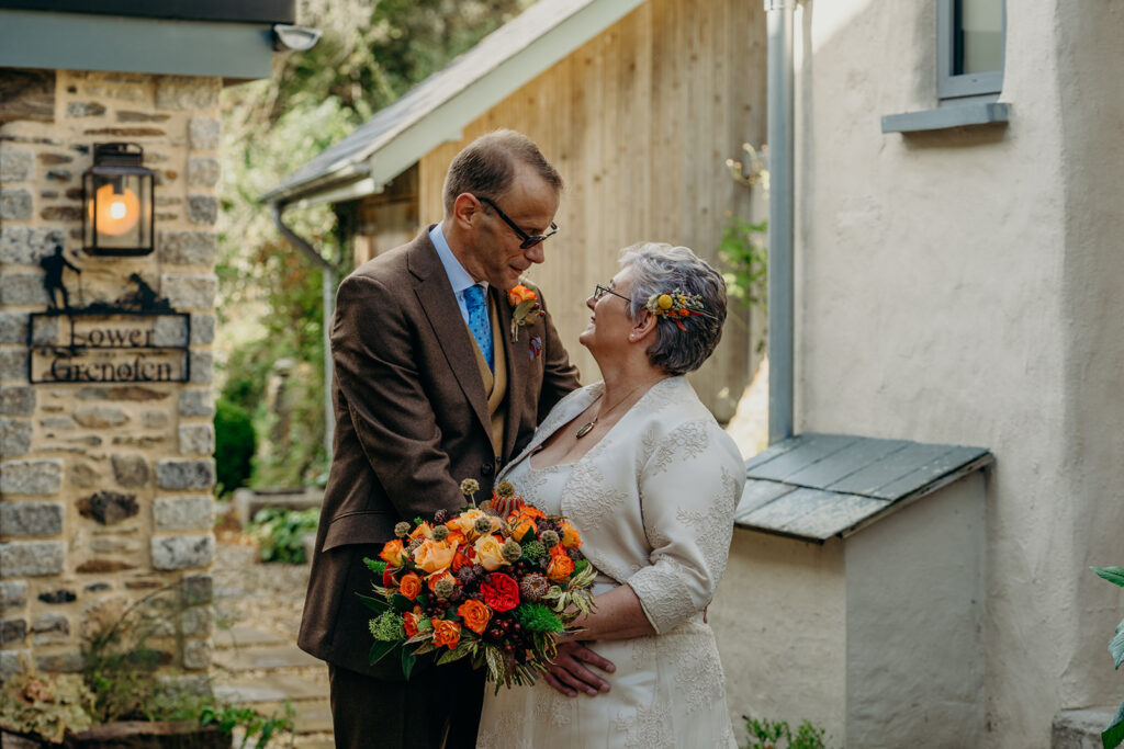 older bride and groom outside in a rustic setting looking at each other bride holding autumn coloured bouquet