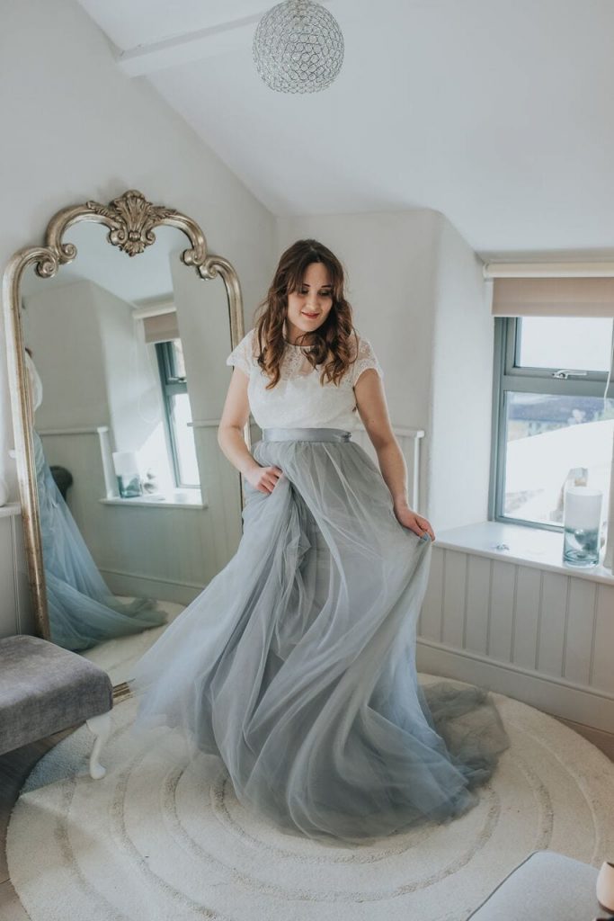 bride in honeymoon cottage swirling her dress in front of the mirror. the skirt is grey chiffon and the top is ivory