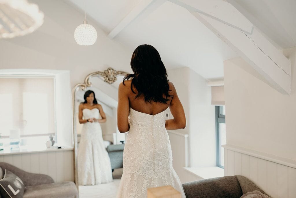 bride looking in mirror. in focus is her back. dress is lacy, strapless and trumpet shaped