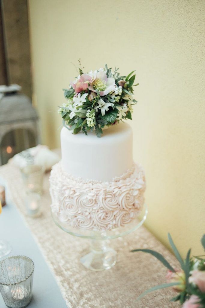 two tier miniature elopement wedding cake with ivory ganache icing on the bottom tier and ivory fondant icing on the top. Decorated with a bunch of blush pink and white flowers with greenery.