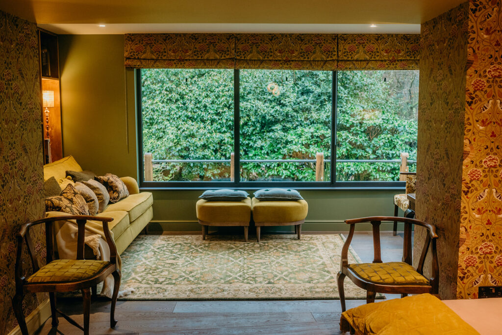 low ceiling country house living room looking out over evergreen planted the room decorated in greens and mustard with William Morris wallpaper in Summer By May in Saffron 