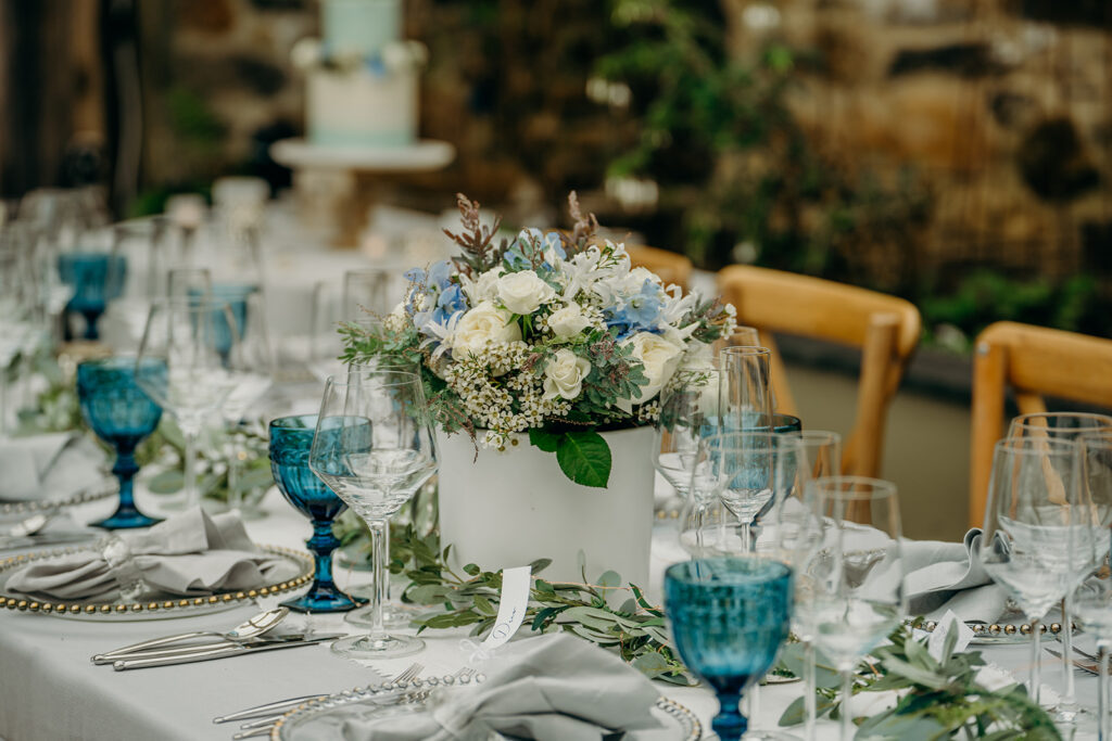 close up of elopement tablescape set with grey table linen crystal glasses and napkin rings and dark blue goblets white and blue fresh flowers