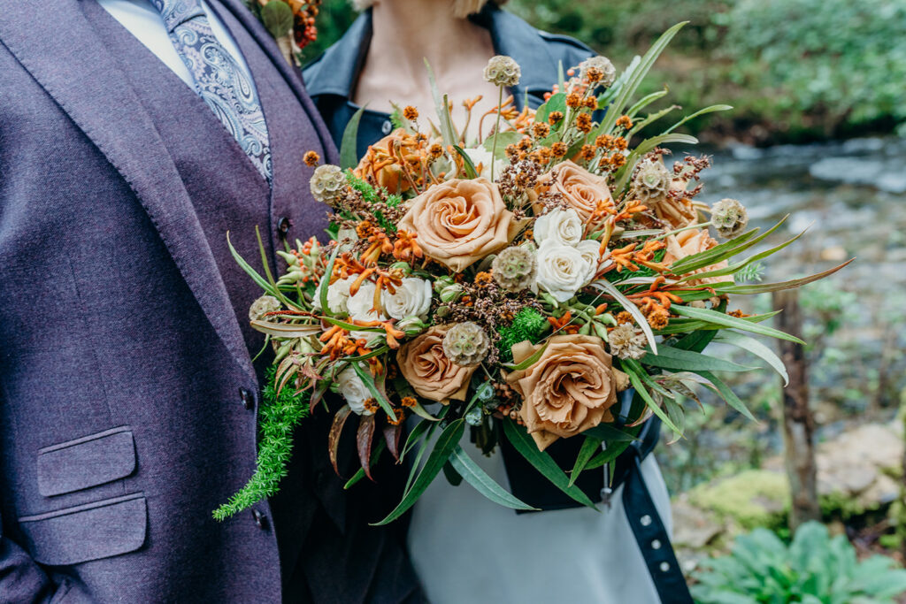 close up mid body shot of wedding couple and bouquet with bronze coloured roses bride wearing black leather jacket