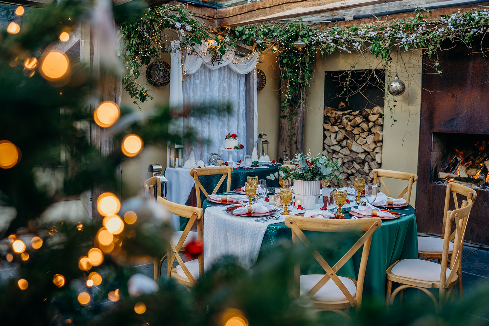 photo of glass roof terrace with oak beams and slate floor open fire set up for Christmas 2023 elopement weddings in dark greens, whites and red with xmas tree in foreground