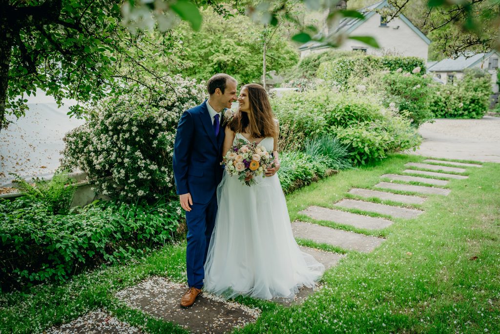 bride and groom outside on a grass path in front of a bank of planting