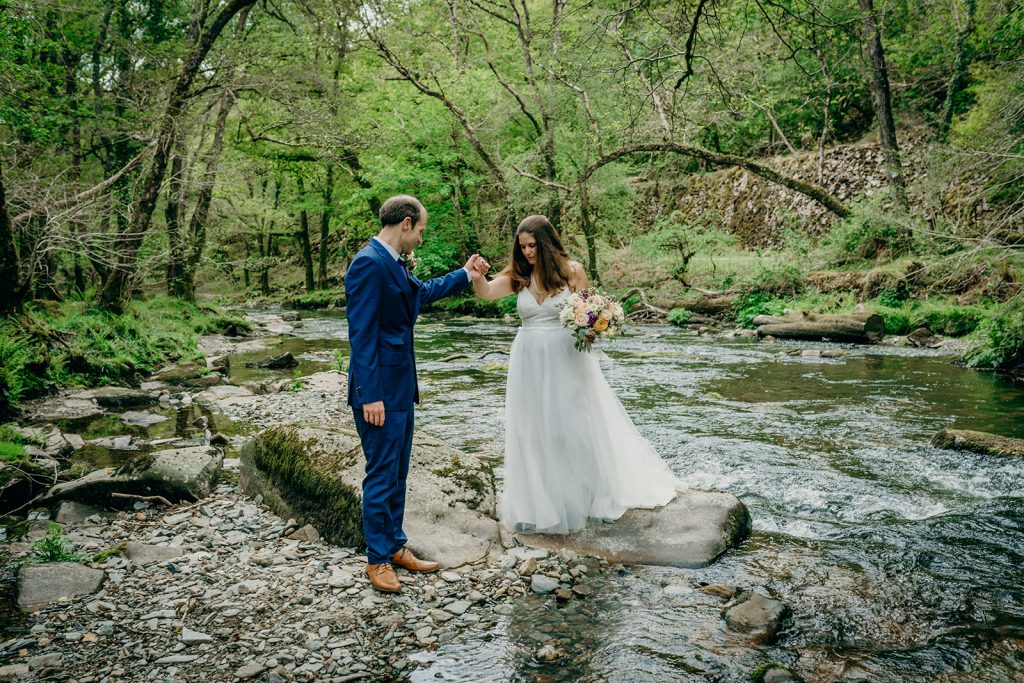 groom helping bride off a rock in a dartmoor river
