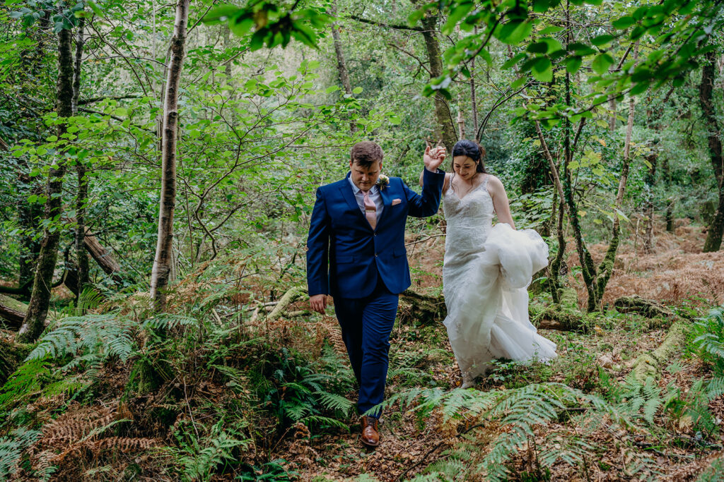 groom leading bride by the hand walking in woodland