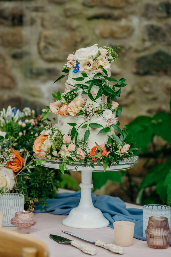 mint iced wedding cake decorated with fresh flowers on a white glass cake stand