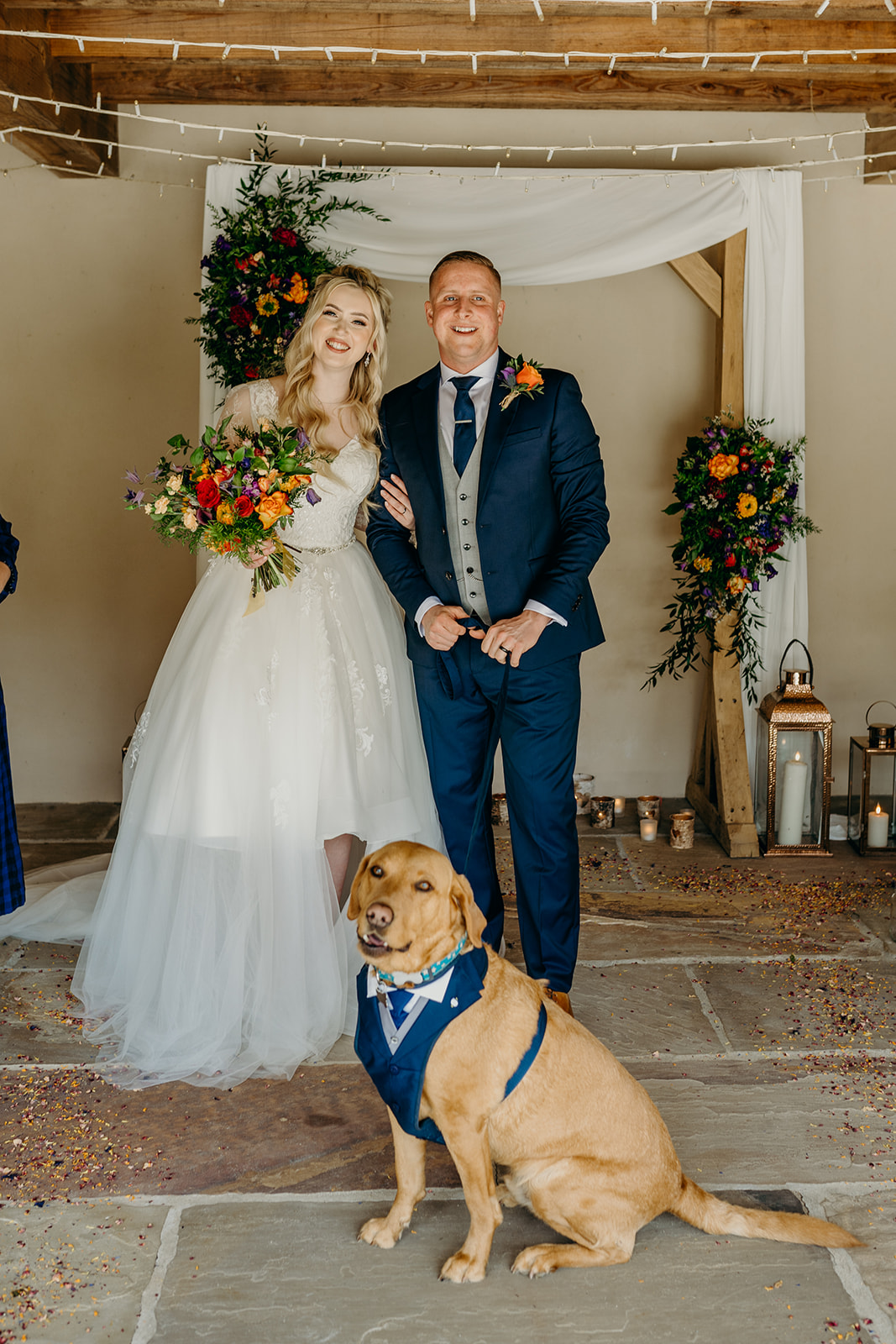can i bring my dog to my wedding bride and groom standing with labrador dog in front of wedding arch