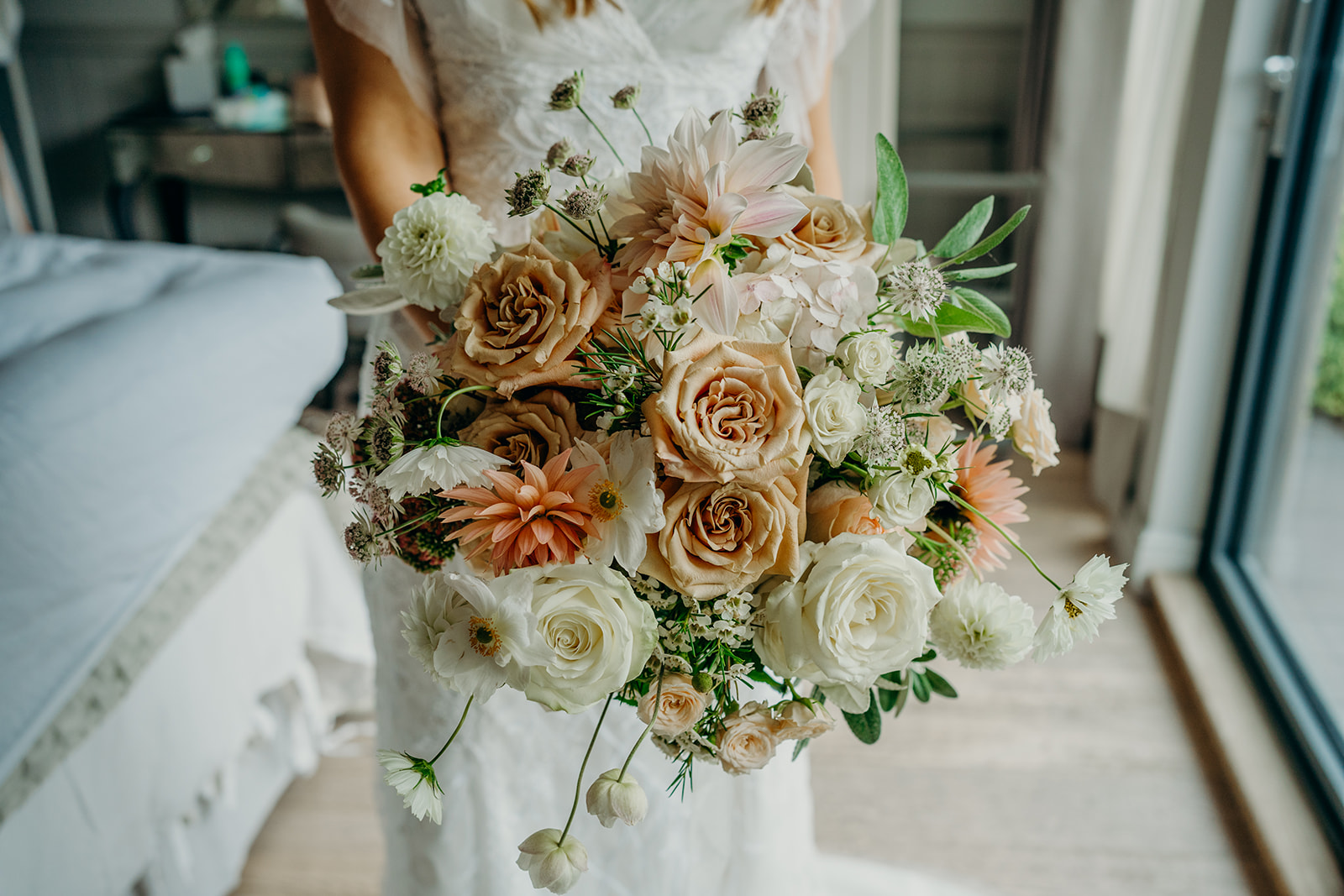 mid section close up of a bride holding a large bridal bouquet with caramel roses, white dahlias and cosmos in nude and blush colours
