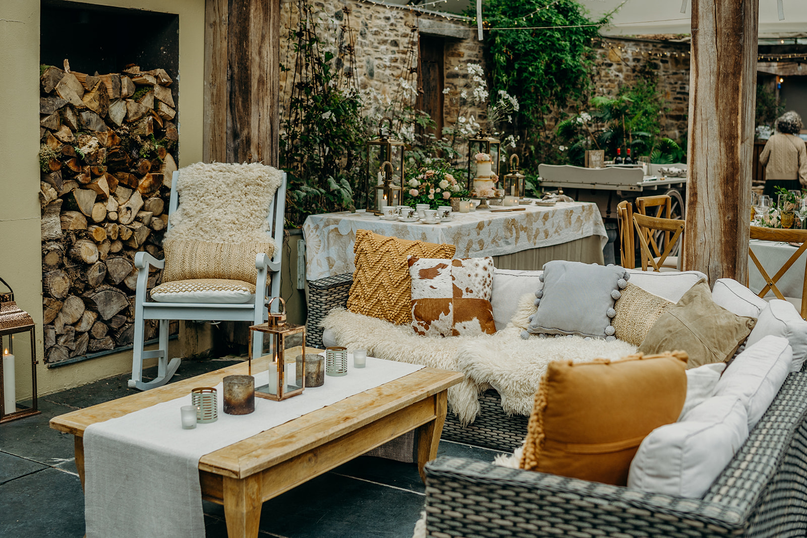photo of an undercover terrace with slate floor and stone wall set up for a rustic wedding with a cake table in coffee and caramel colours