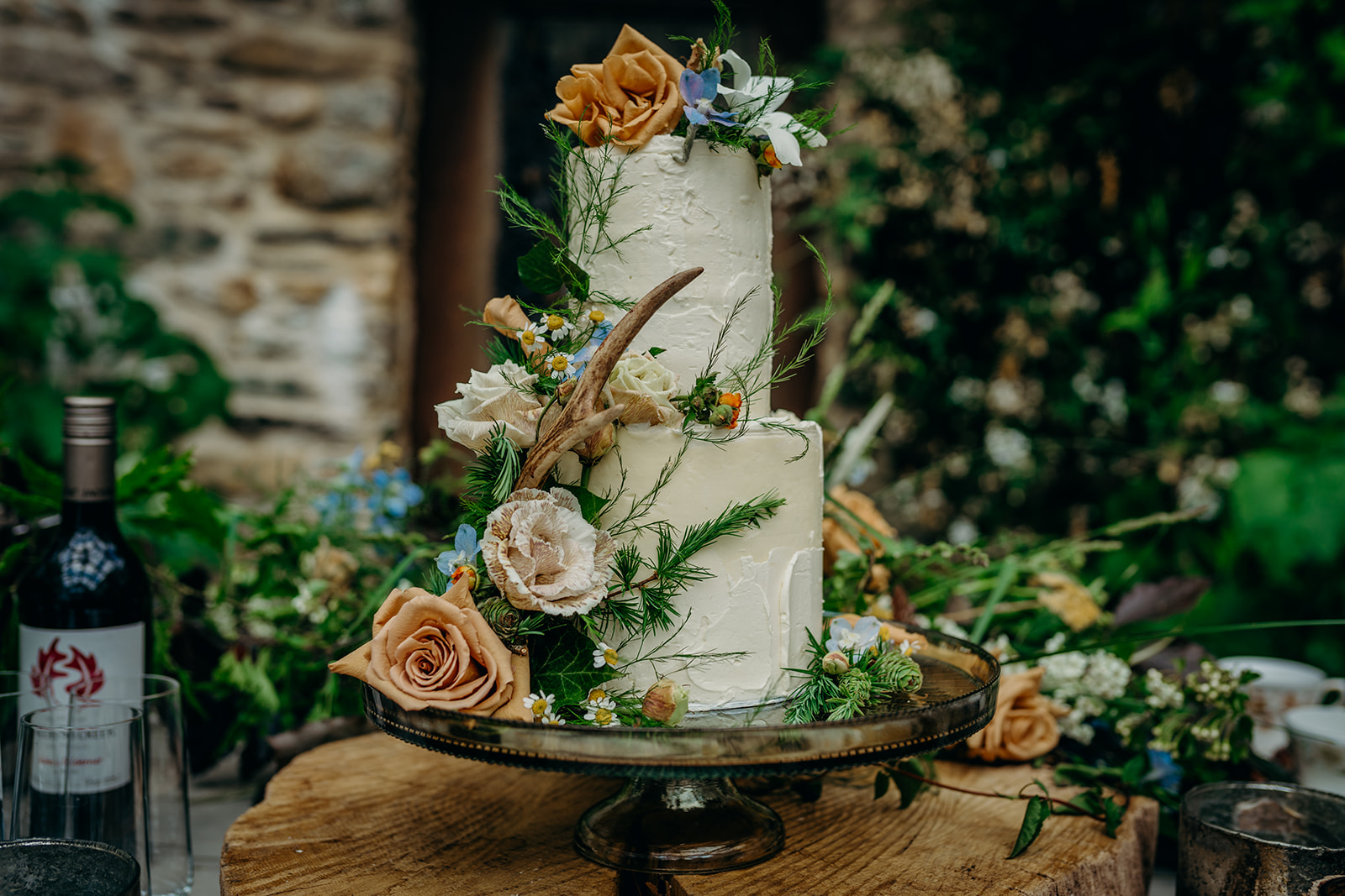 elopement wedding cake decorated with toffee roses, pale blue flowers on a cake stand on a log slice