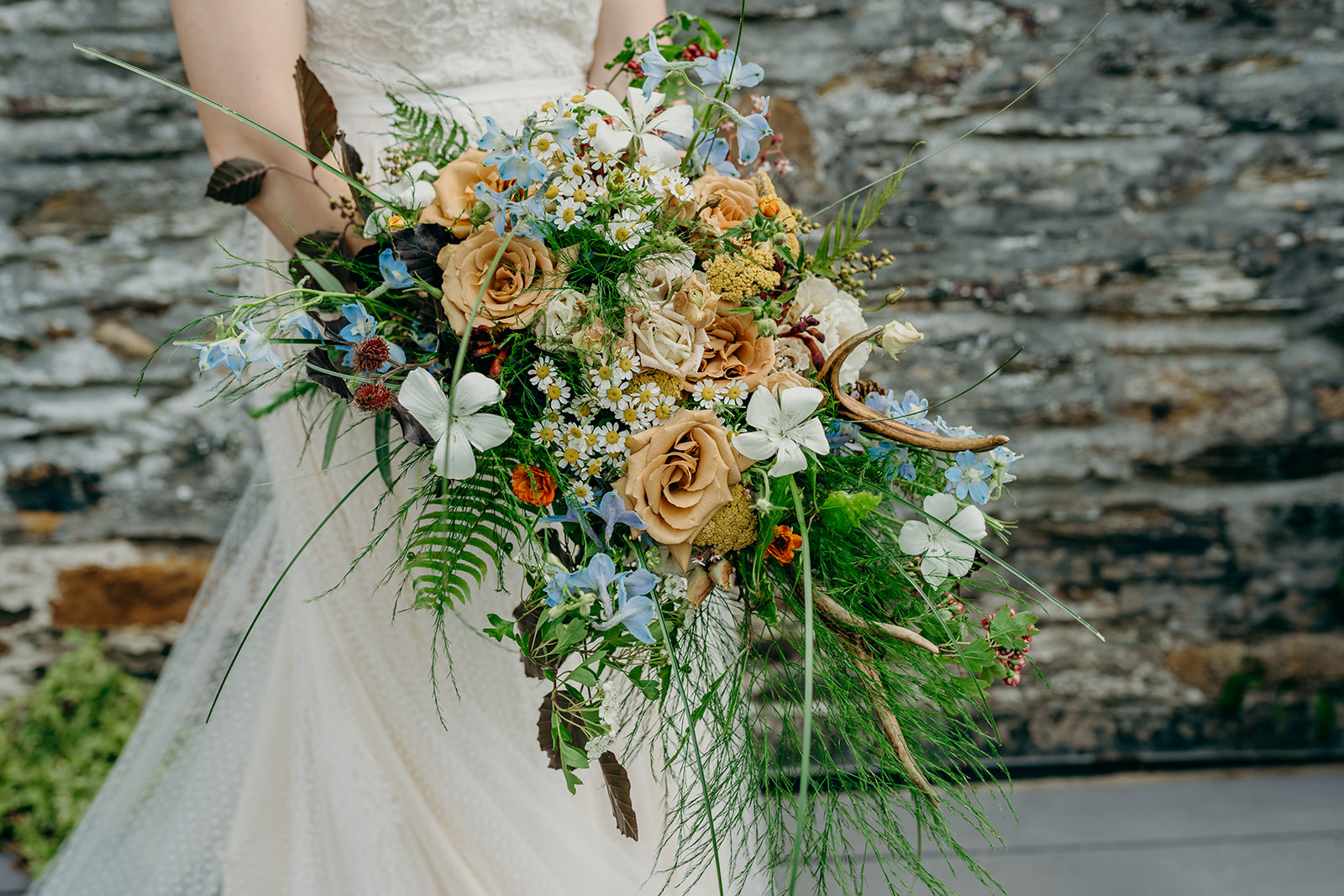 mid section shot of a bride in a white dress holding a large wild bridal bouquet with colours of toffee, white and pale blue 