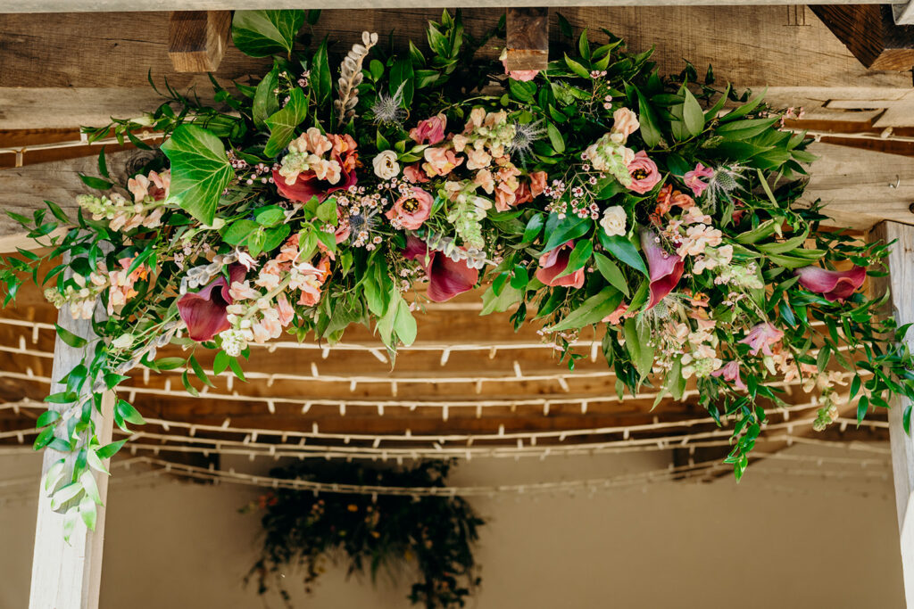 oak frame decorated with flower arch in shades of pink with fairy lights behind