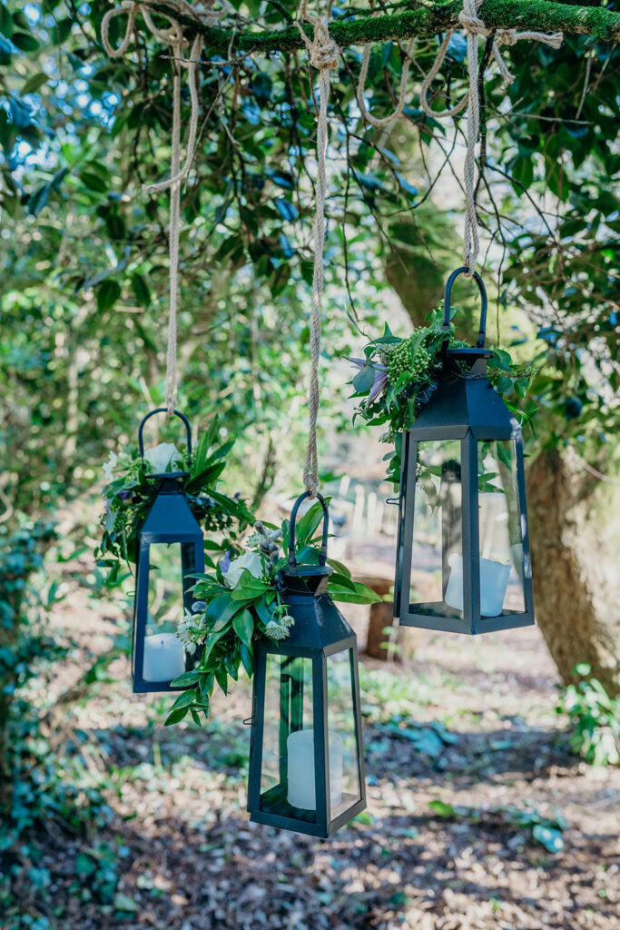 3 black lanterns hanging from a willow tree with string and flowers 