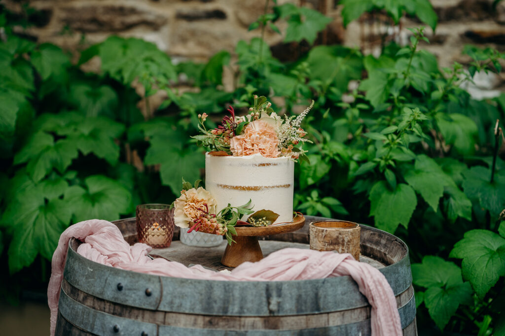 small elopement wedding cake on an oak barrel with blush pink drapery decorated with fresh flowers