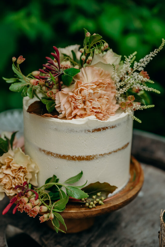 small semi naked elopement wedding cake on a wood cake stand decorated with fresh flowers in peach