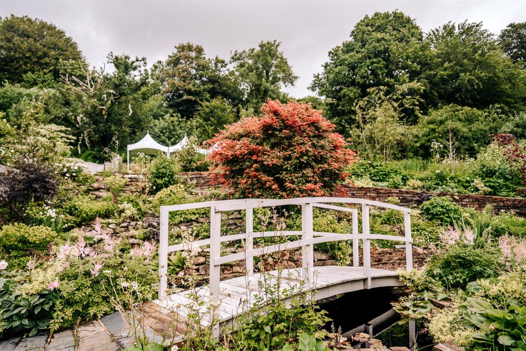 wooden bridge over a lily pond set in landscaped gardens in the Devon countryside with a marquee in the background