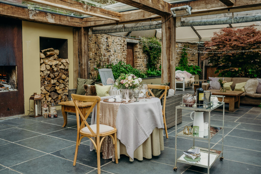 glass roof oak frame terrace with log store and wedding table set up for two with drinks trolley and flower beds in the background 
