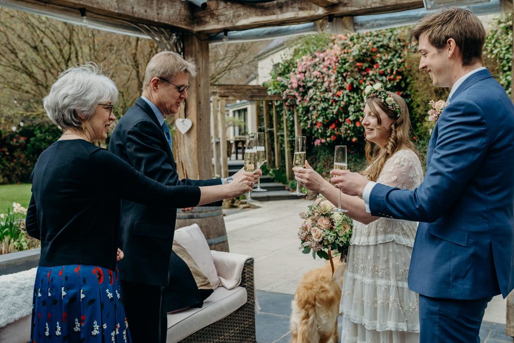 bride and groom chinking champagne flutes with wedding guests outside