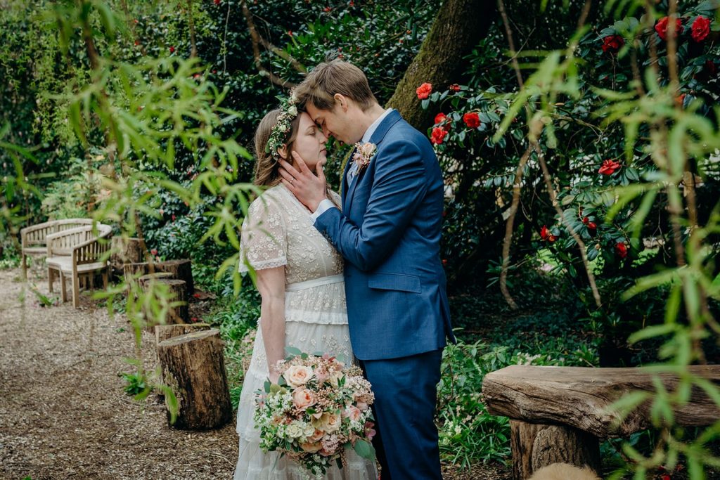 bride and groom in landscaped gardens with red camellias touching foreheads