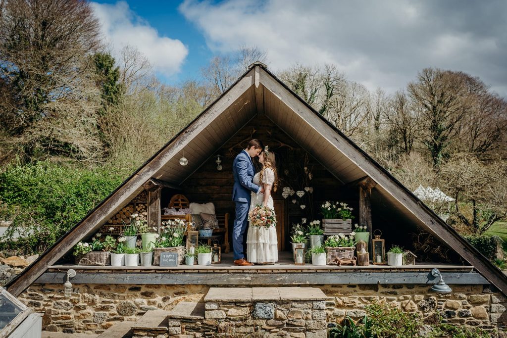 bride and groom in oak frame apex with clouds and blue sky ahead and spring bulbs in pots