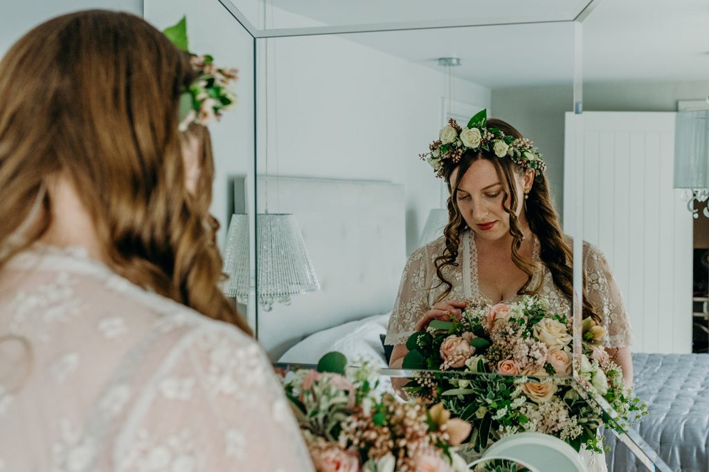 bride with half head flower crown and bridal bouquet of ivory and blush roses reflected in a mirror