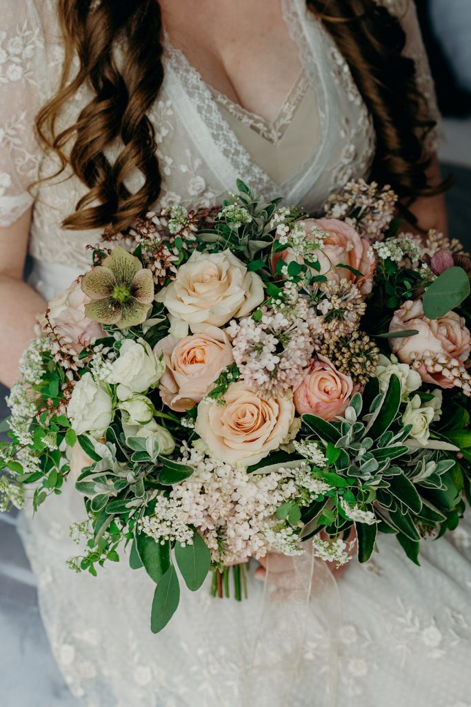 close up of bride holding bouquet of blush and ivory roses hellebores lilac and pieris