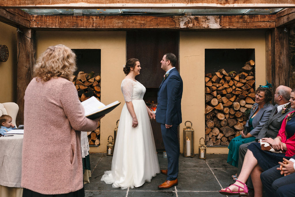 bride and groom getting married stood facing each other in front of fire under glass roof 