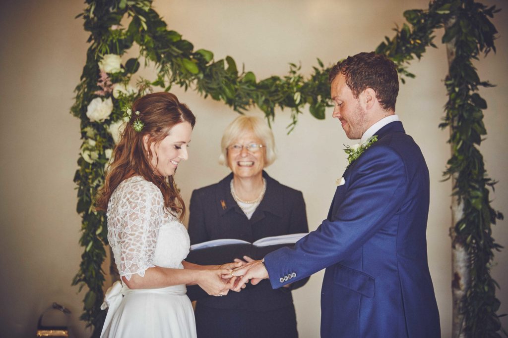 bride and groom wedding ceremony with celebrant & rustic arch with foliage garland backdrop