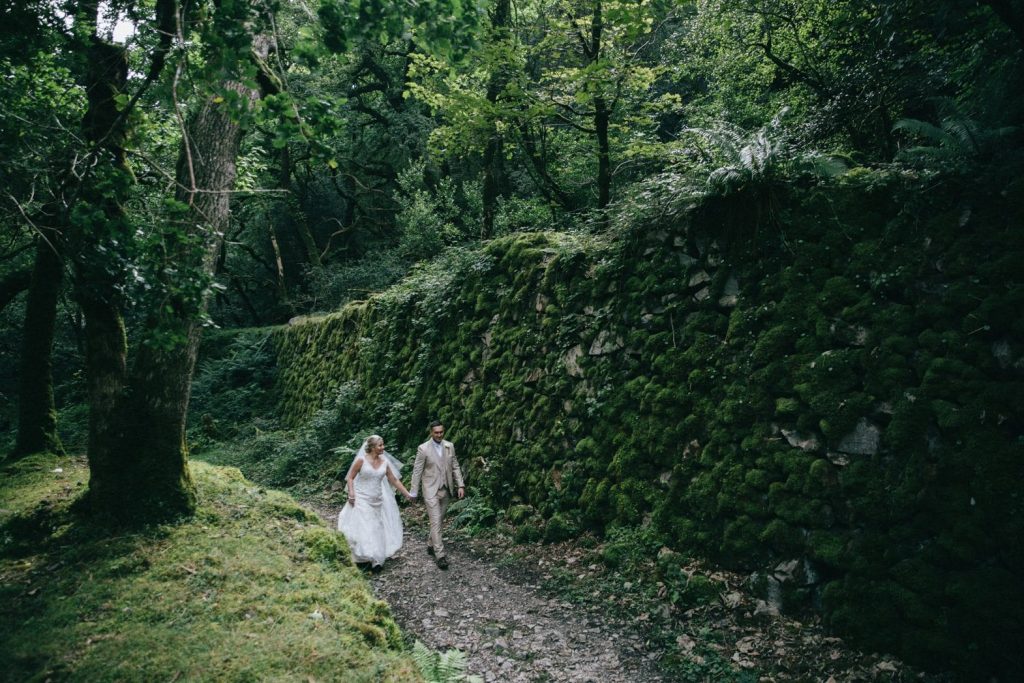 bride and groom woodland walk by moss covered wall