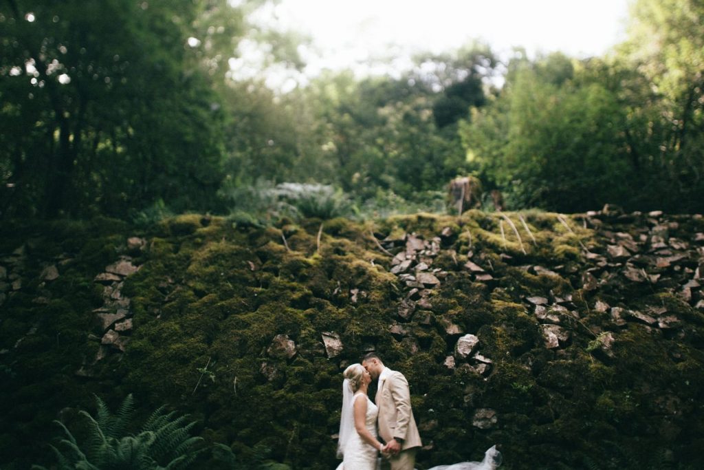 bride and groom kissing by moss covered woodland wall