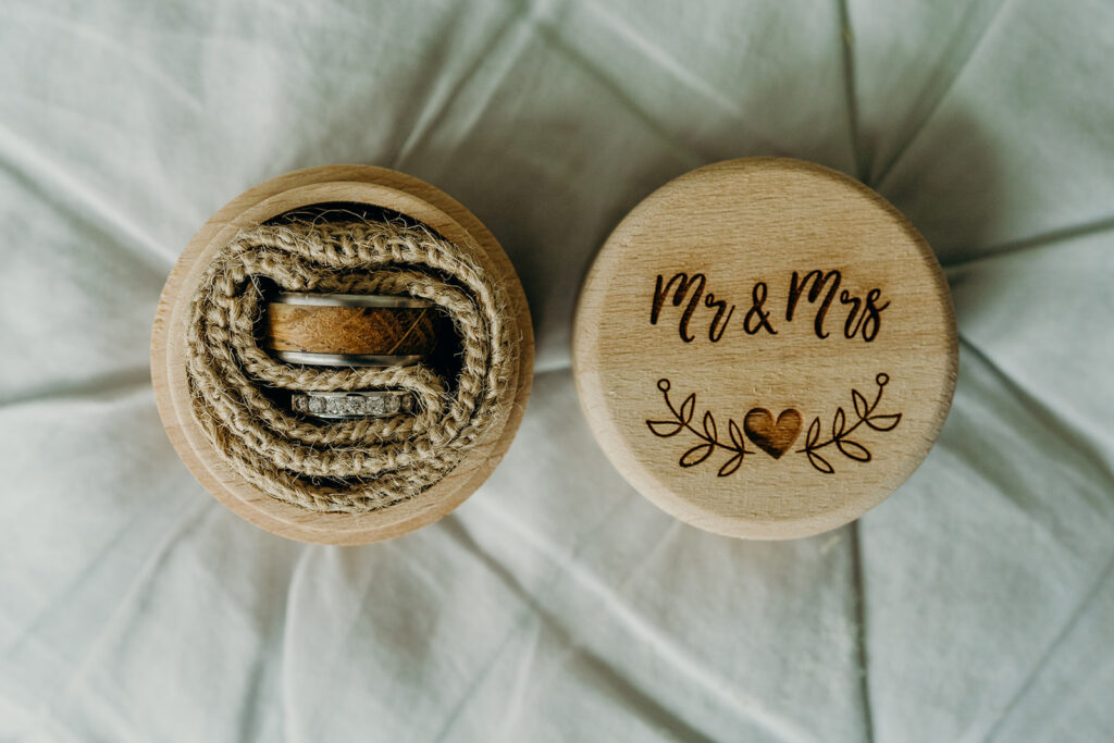 close up of a round wooden ring box engraved Mr and Mrs with wooden and steel ring and a diamond ring