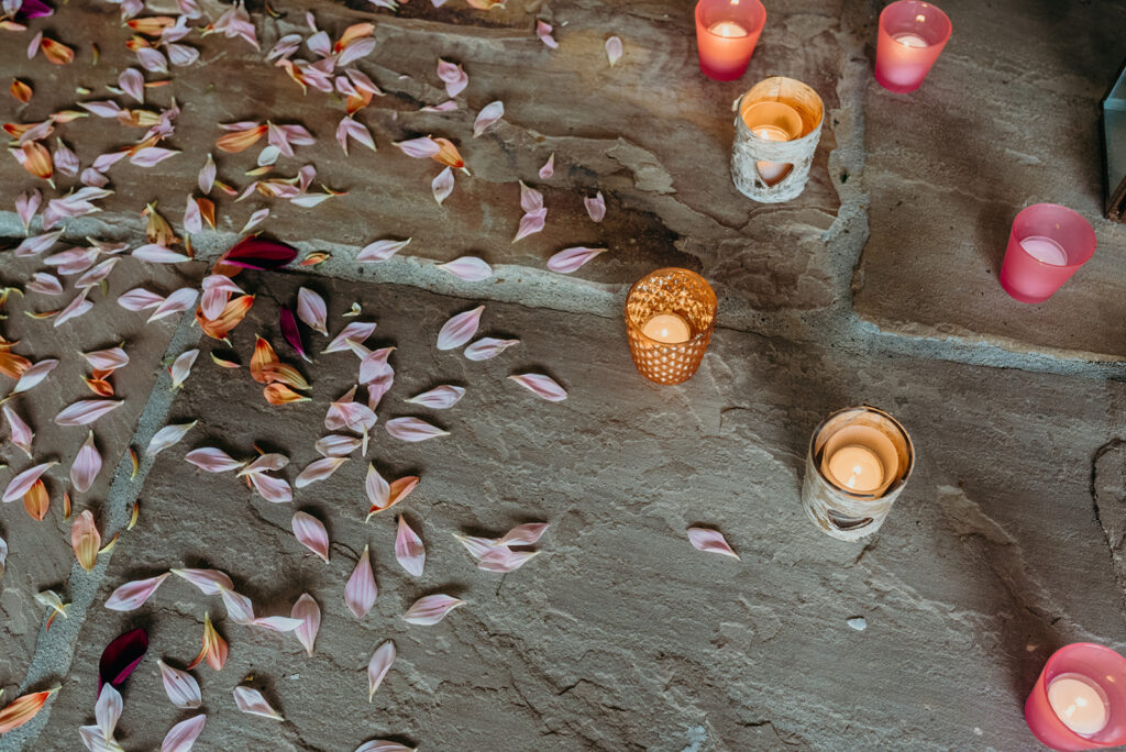 overhead shot of a rustic stone floor with pink flower petals and pink and orange tealights