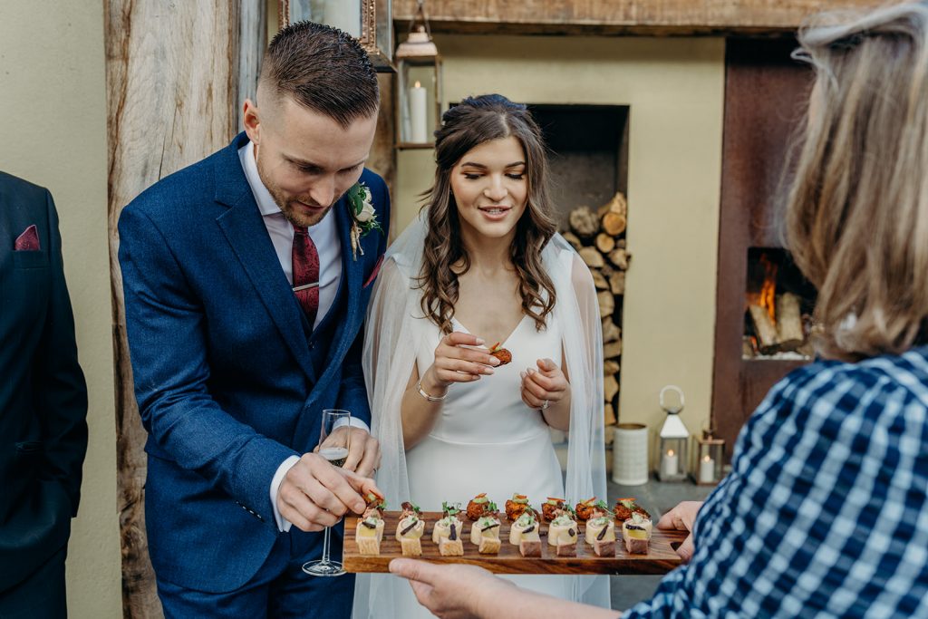 bride and groom looking at a tray of canapes on a wooden board held by a server 