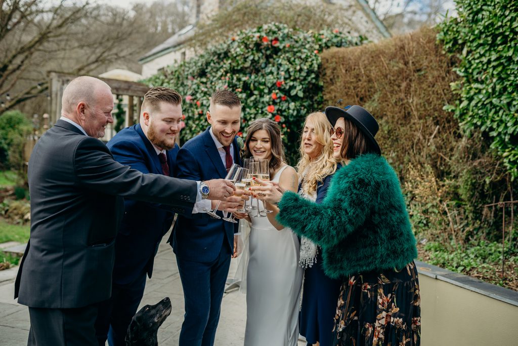 bride and groom clinking glasses with wedding guests outside in landscaped gardens in the winter