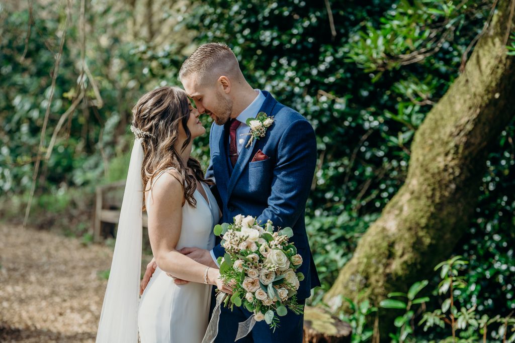 bride and groom touching foreheads outside by a tree trunk with greenery in the background