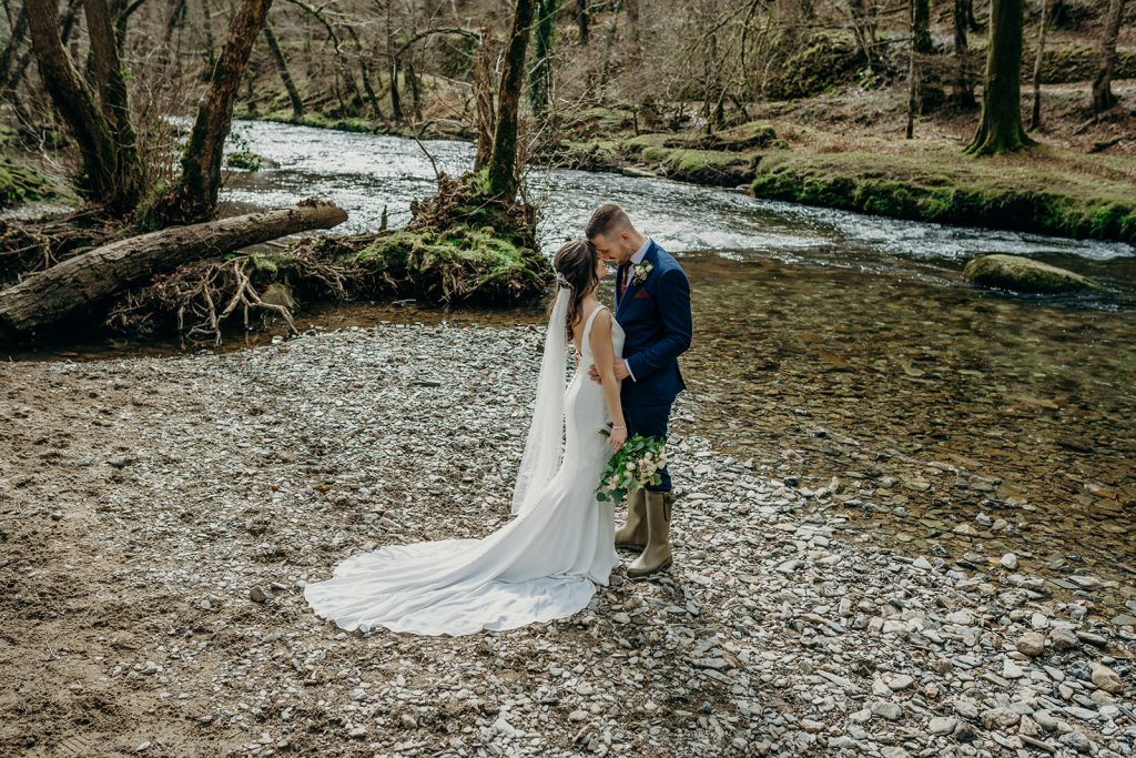 bride and groom stood on the banks of a dartmoor river touching foreheads