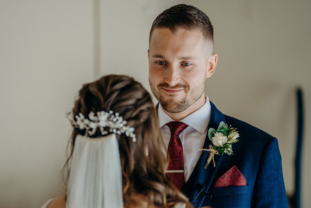 groom looking at bride wearing blue suit white shirt burgundy tie and pocket square with white rose buttonhole