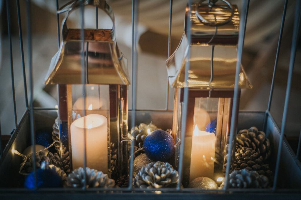 candles in lanterns sitting in a metal cage with pine cones, baubles, and fairy lights to decorate