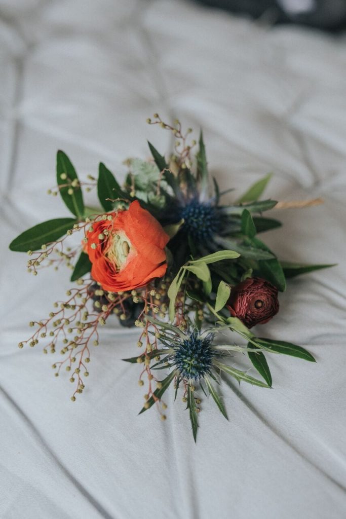 close-up of buttonhole make up of red flower and thistles plus greenery 