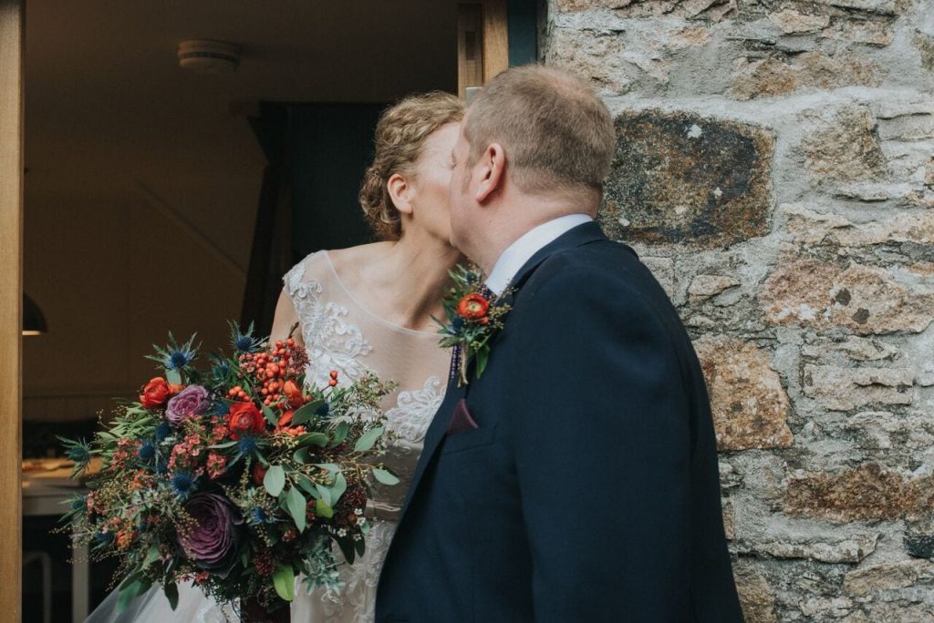 bride and groom sharing a kiss as they see each other for the first time on their wedding day. the bouquet and the buttonhole are showcased next to each other.