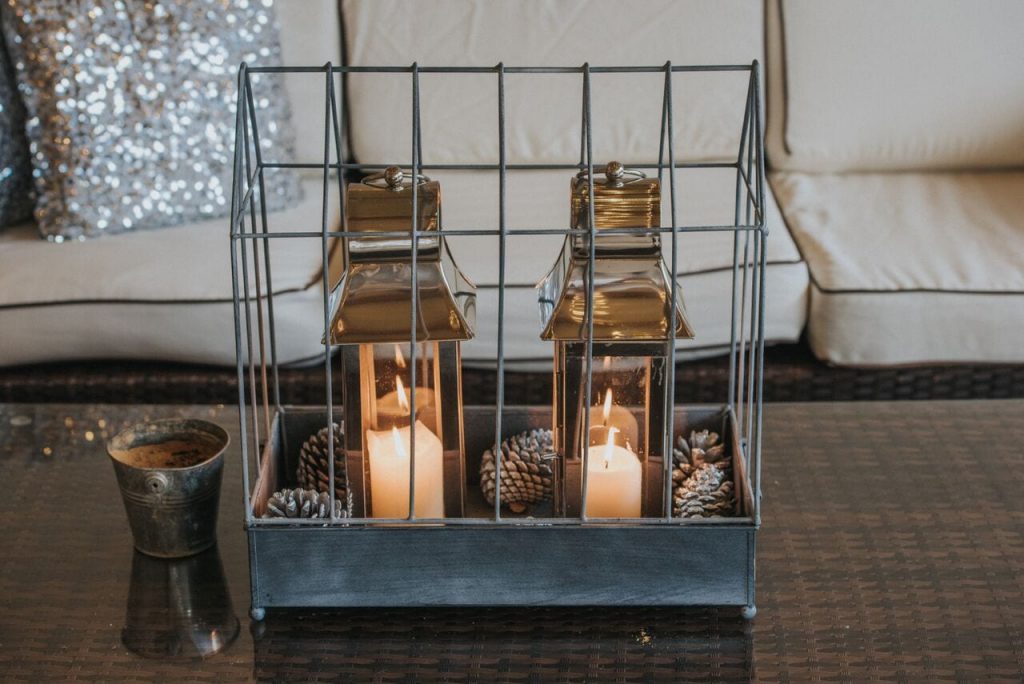 candles in lanterns sitting in a metal cage with pine cones to decorate