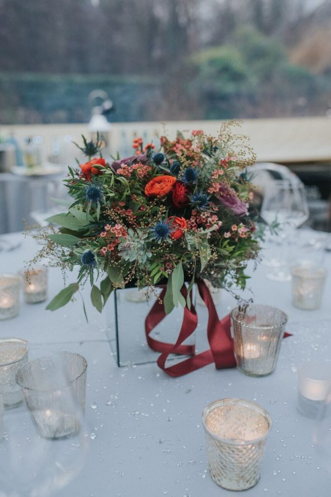 close up of the bride's red, purple, navy and green bouquet as the centrepiece of their wedding breakfast table 