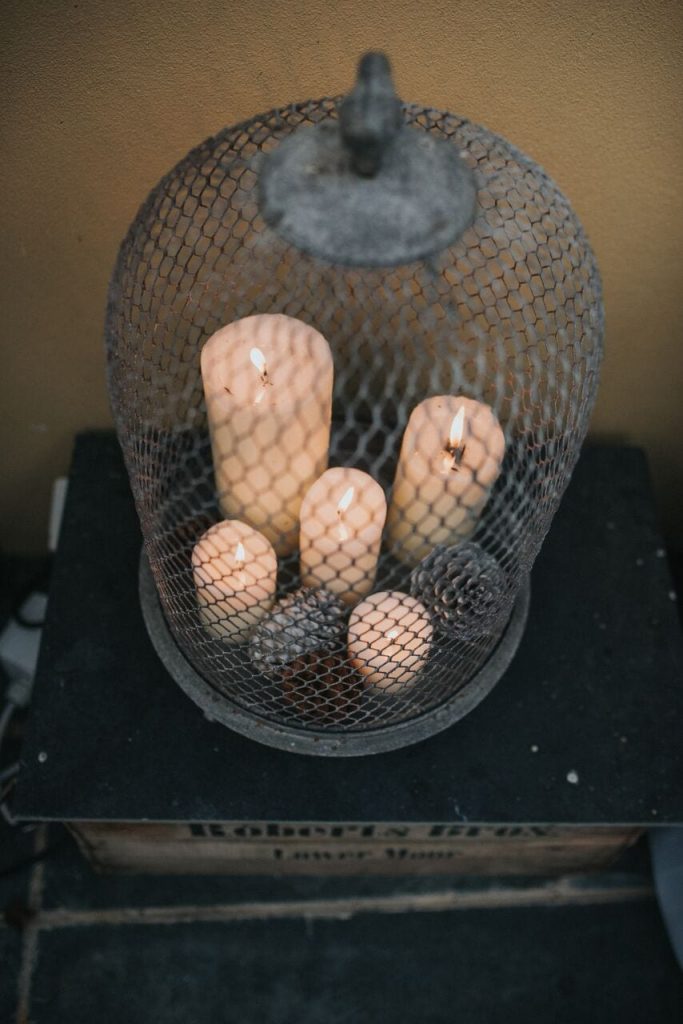 close up of various sizes candles and pine cones in a metal birdcage container 