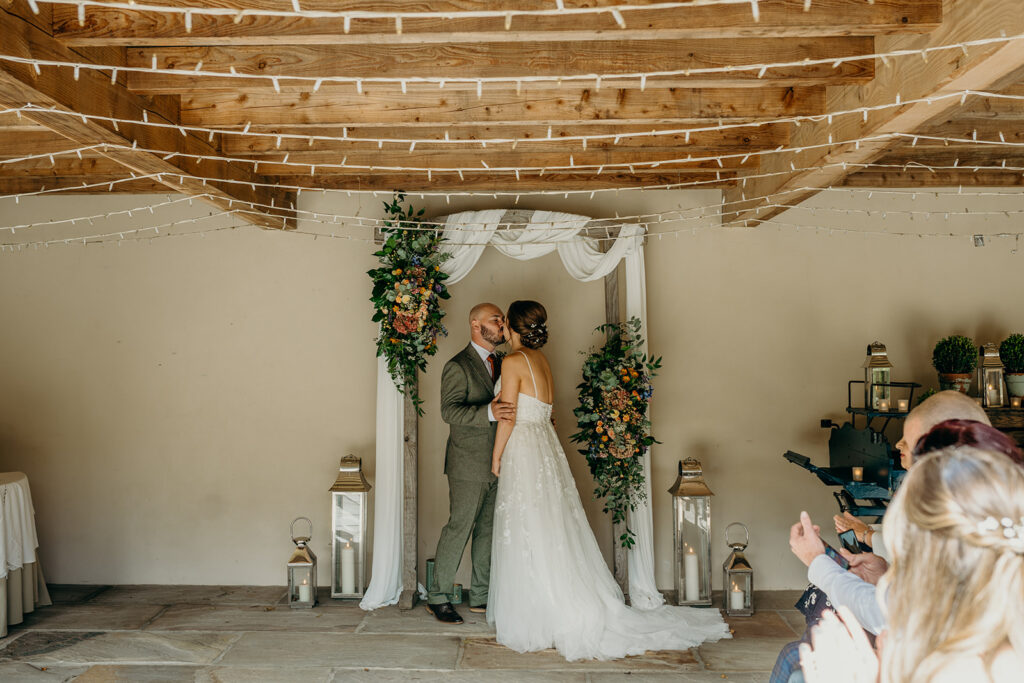 bride and groom kissing in front of wedding arch after ceremony