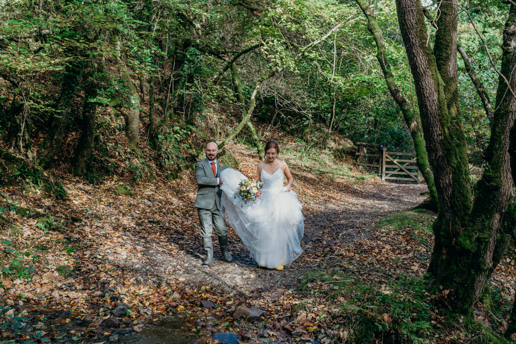 bride and groom walking in woods groom carrying bridal train