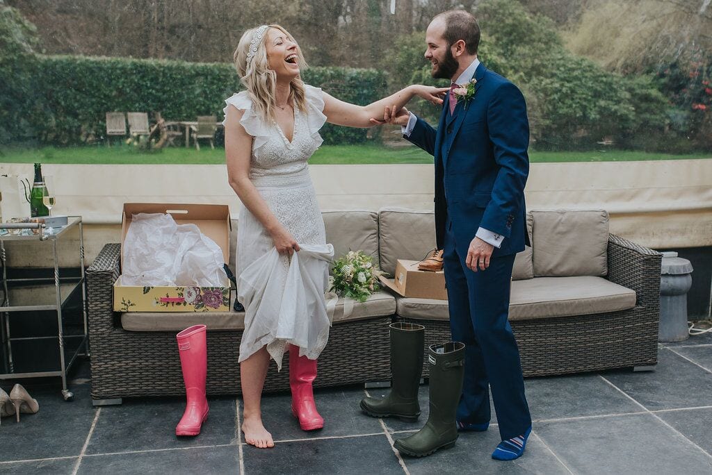 bride holding grooms shoulder for support as they laugh at them both putting their wellington boots on